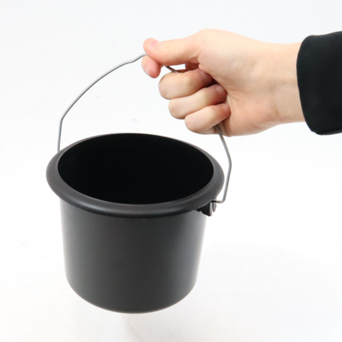Black bucket with handle held by a hand on a white background