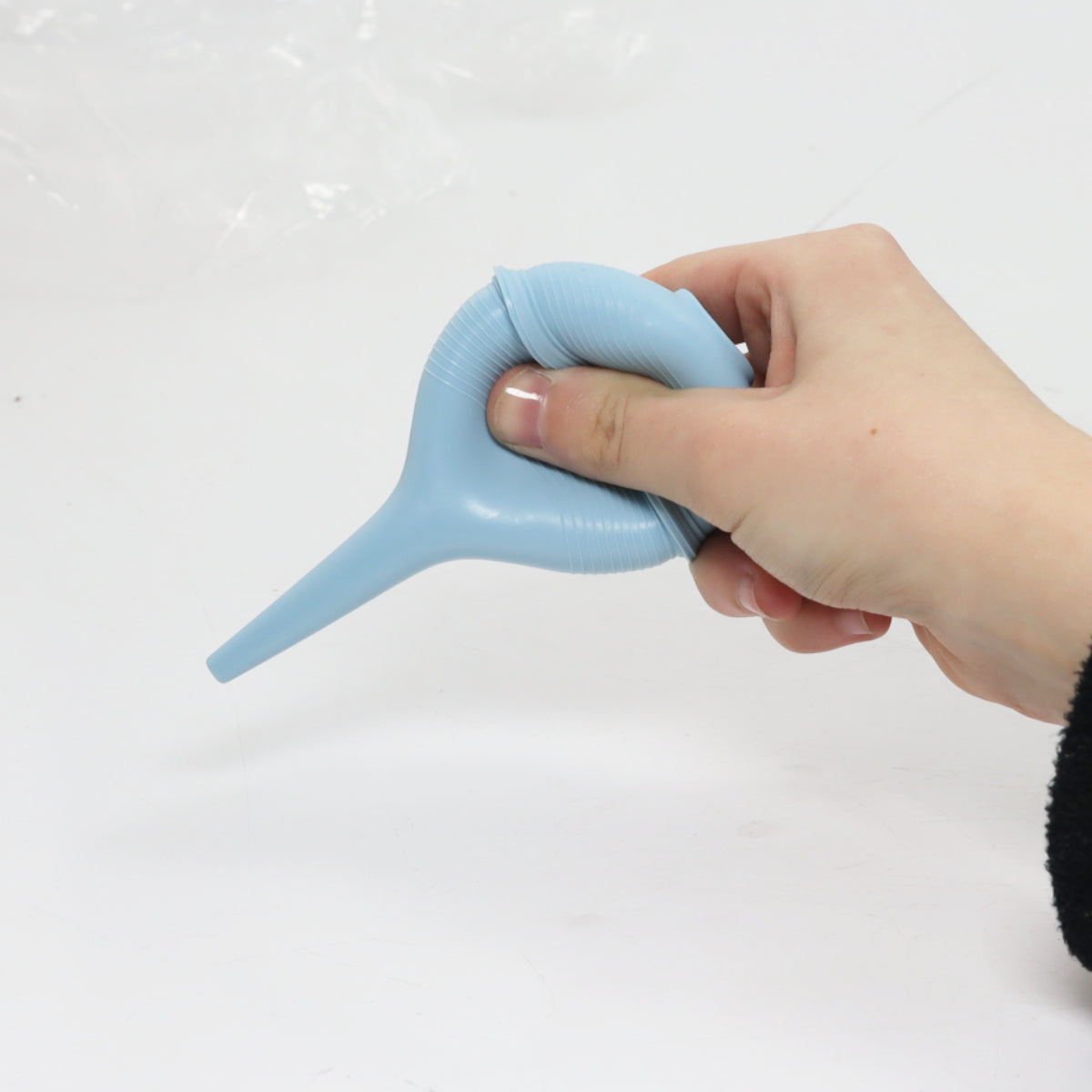 Hand holding a blue silicone bulb syringe against a white background