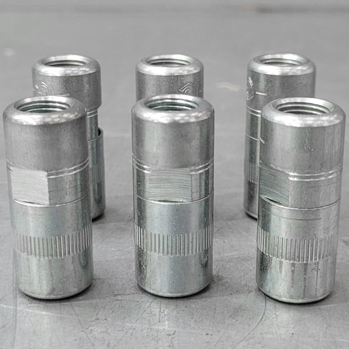 Set of six metal cylindrical components on a gray surface