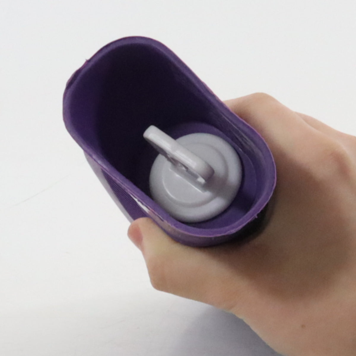 Hand holding a purple container with a white lid on a light gray background