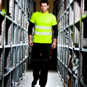 Person wearing a high-visibility safety vest walking through an aisle of shelves.