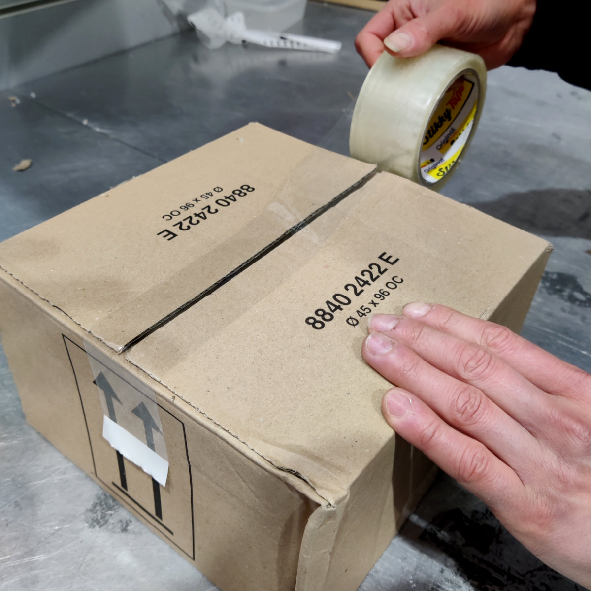 Person sealing a cardboard box with tape on a concrete floor.