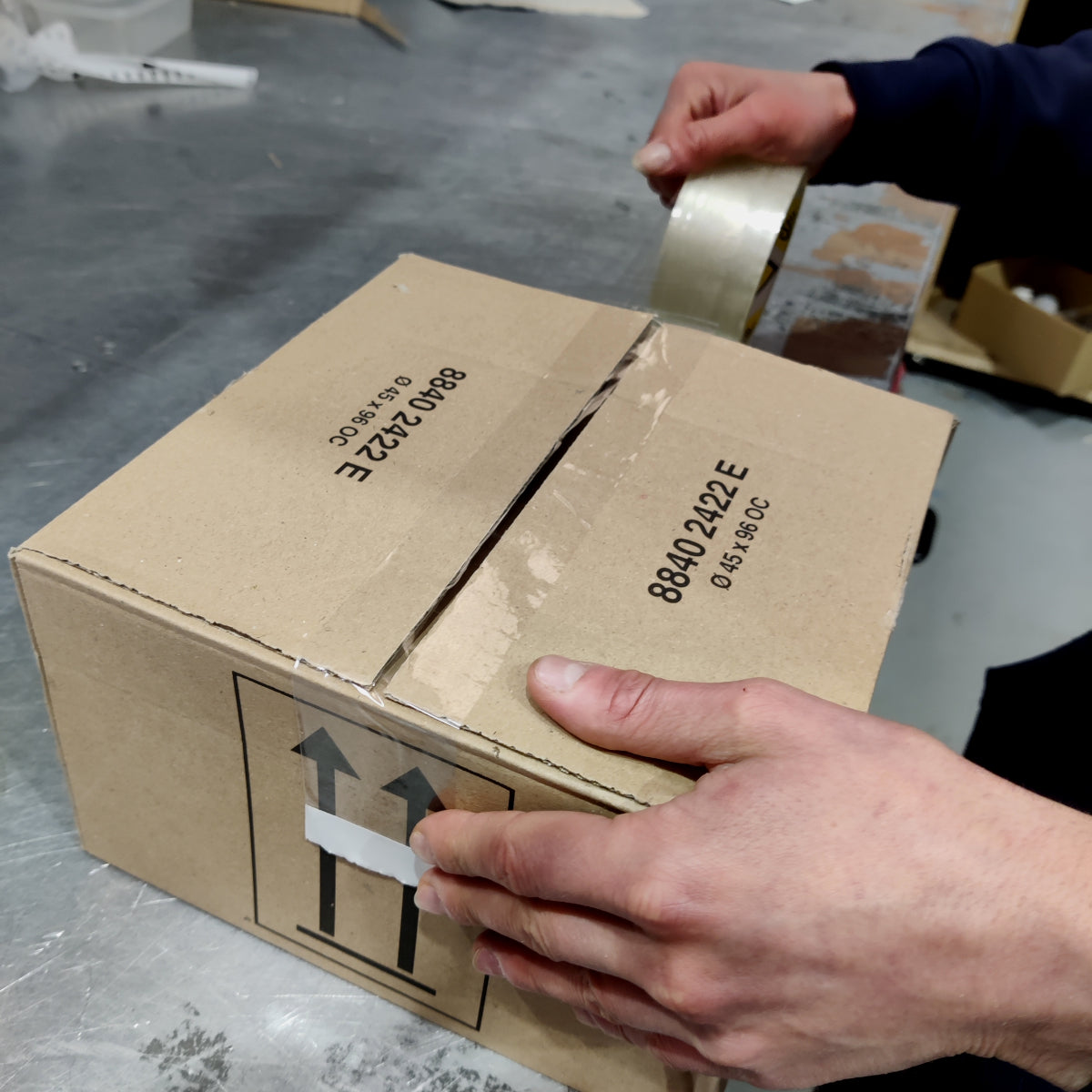 Person taping a cardboard box closed on a concrete floor.