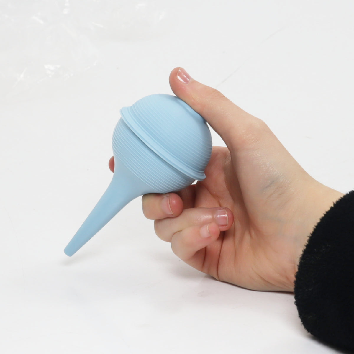Hand holding a blue silicone bulb syringe against a white background
