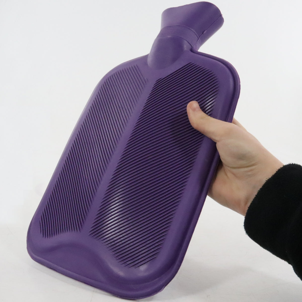 Purple hot water bottle held by a hand on a white background