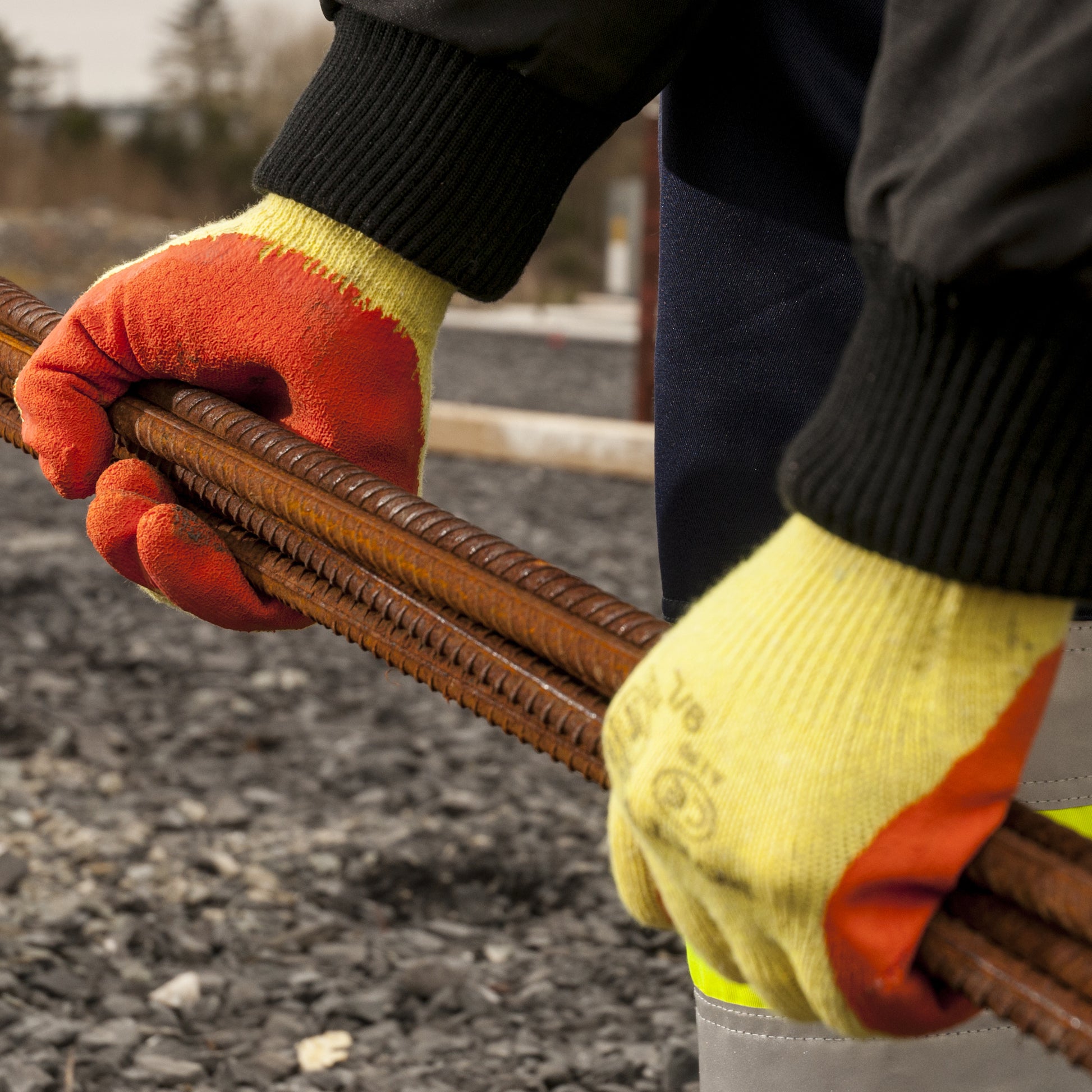 Close-up of gloved hands holding a rusty metal rod on a construction site.